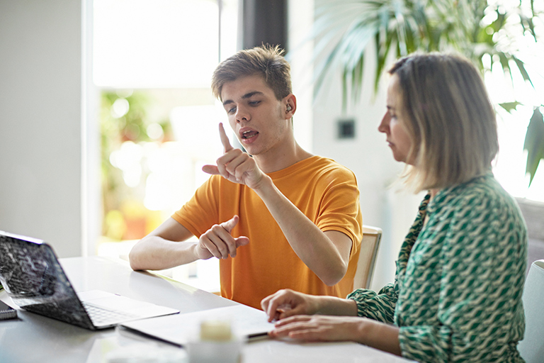 young man signing to woman at desk while sitting in front of computer